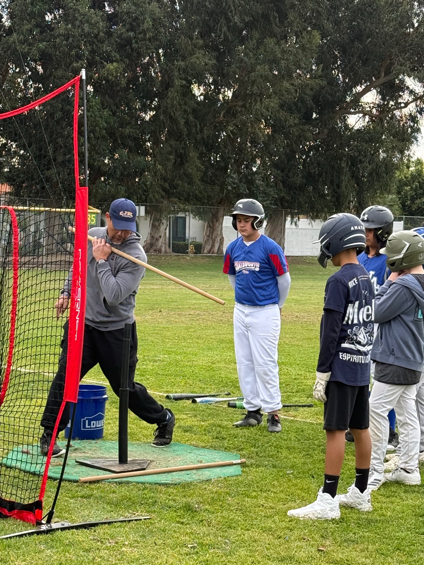 Coach demonstrating batting technique to group of youth baseball players